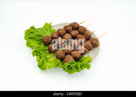 Leckere gebratene Rindfleischspieße und Salat auf Gericht mit weißem Hintergrund. Fleischbällchen aus Fleisch. Asiatisches Street Food. Leckeres gegrilltes Rindfleisch Stockfoto