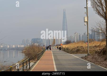 Blick auf einen Fußgänger- und Fahrradweg im Jamsil Hangang Park mit dem majestätischen Wolkenkratzer Lotte World Tower im Hintergrund Stockfoto