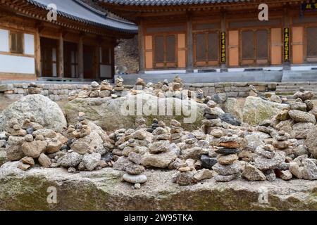 Kleine Türme aus Kieseln und Felsen, die von vorbeifahrenden Wanderern mit historischen koreanischen Gebäuden im Hintergrund im Bukhansan-Nationalpark gebaut wurden Stockfoto