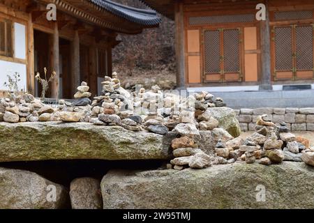 Kleine Türme aus Kieseln und Felsen, die von vorbeifahrenden Wanderern mit historischen koreanischen Gebäuden im Hintergrund im Bukhansan-Nationalpark gebaut wurden Stockfoto