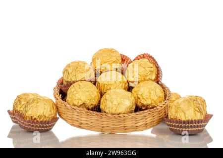 Mehrere Pralinen in einer Papierverpackung auf einer Strohplatte, Makro, isoliert auf weißem Hintergrund. Stockfoto