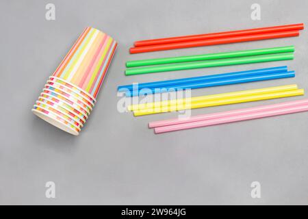 Bunte Pappbecher und bunte Plastikhalme für Getränke. Grauer Hintergrund. Flache Lagen. Wiederverwendung, Umweltkonzept. Stockfoto