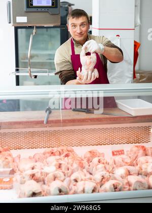Ein positiver Verkäufer bietet an, Hühnerschlachtkörper im Lebensmittelgeschäft zu kaufen Stockfoto