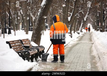 Kommunaler Arbeiter in Uniform mit Schaufel räumt Schnee auf einem Bürgersteig ab. Mann bei Schneeräumung in der Winterstadt, Straßenreinigung Stockfoto