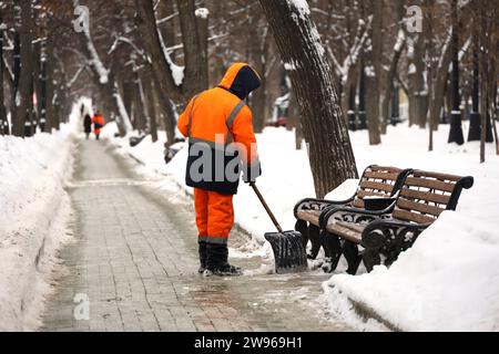 Kommunaler Arbeiter in Uniform mit Schaufel räumt Schnee auf einem Bürgersteig ab. Mann bei Schneeräumung in der Winterstadt, Straßenreinigung Stockfoto