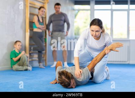 Beim Selbstverteidigungstraining vermittelt der Trainer Frauen die Technik, den Arm zu greifen und den Gegner auf den Boden zu senken Stockfoto