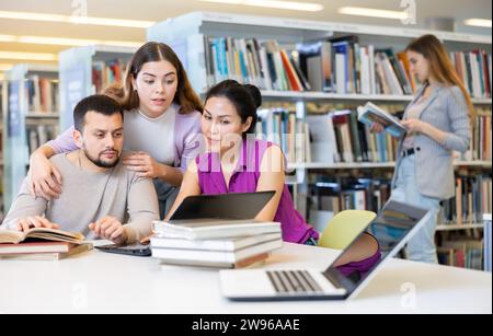 Drei Erwachsene Schüler arbeiten an einem Laptop und lesen Bücher in einer öffentlichen Bibliothek Stockfoto
