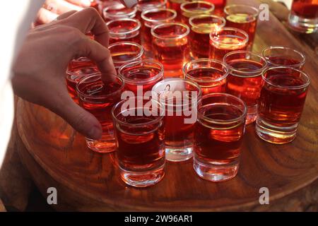 Rote Alkoholtinktur in kleinen Gläsern wird von Menschen zerlegt. Alkoholische hausgemachte Getränke. Stockfoto