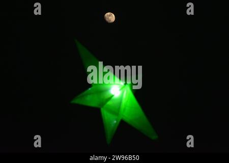 Srinagar, Indien. Dezember 2023. Der Mond steigt während der Weihnachtsfeier in Srinagar über dem Weihnachtsstern der katholischen Kirche der Heiligen Familie auf. (Foto: Saqib Majeed/SOPA Images/SIPA USA) Credit: SIPA USA/Alamy Live News Stockfoto