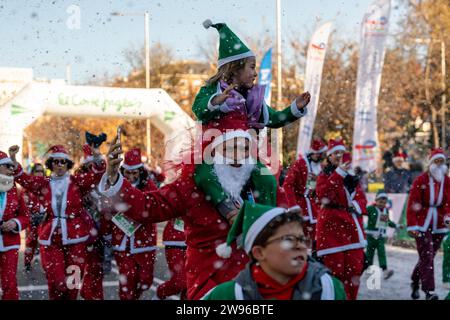 Madrid, Spanien. Dezember 2023. Ein als Weihnachtsmann gekleideter Mann mit einem Kind auf den Schultern kommt während des traditionellen Weihnachtsmannsrennens an der Ziellinie an. Ein jährliches Benefizrennen, das in diesem Jahr dem Spanischen Roten Kreuz helfen wird. (Credit Image: © Guillermo Gutierrez/SOPA Images via ZUMA Press Wire) NUR REDAKTIONELLE VERWENDUNG! Nicht für kommerzielle ZWECKE! Stockfoto