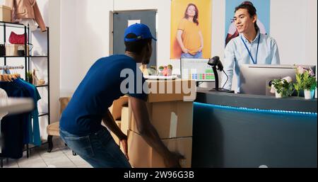 afroamerikanischer Kurier zeigt dem Mitarbeiter einen Lieferbericht an und bittet ihn um Unterschrift. Er bespricht Online-Bestelldetails in einer modernen Boutique. Asiatischer Mitarbeiter, der Kundenpakete für den Lieferer vorbereitet Stockfoto