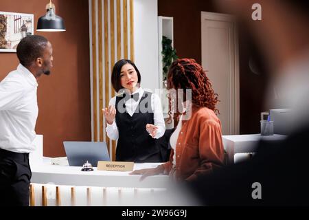 Mitarbeiter, die sich an der Rezeption in der Lobby mit Pärchen unterhalten und Gästen luxuriösen Service bieten. Asiatische Rezeptionistin begrüßt die Leute in einem modernen, teuren Hotel und meldet sich am Eingang an. Stockfoto