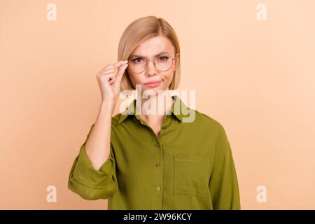 Foto einer unzufriedenen verdächtigen Frau mit bob-Frisur gekleideten grünen Hemdfingern halten Brillen isoliert auf beigefarbenem Hintergrund Stockfoto