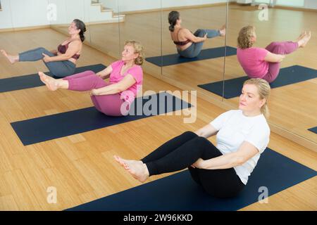 Drei reife europäische Frauen spielen in einem Fitnessraum eine Bootsstellung Stockfoto