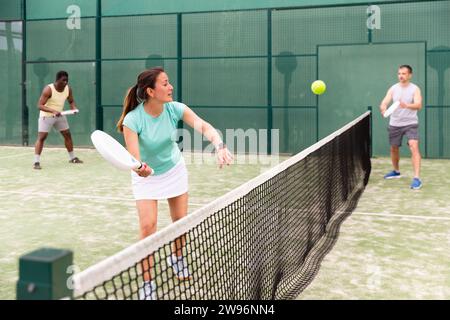 Porträt einer jungen Frau, die beliebte Schlägersportpadel genießt und Doppel-Match mit männlichen Freunden auf dem Platz im Freien spielt Stockfoto