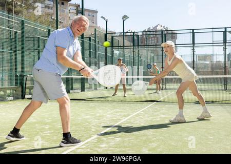 Motivierter Senior-Mann und -Frau spielen Padel mit seinem Teamkollegen vor Gericht Stockfoto