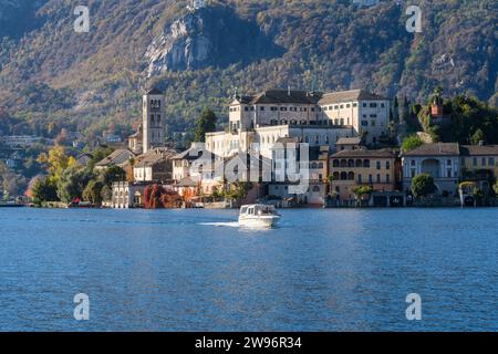 San Giulio Island im Orta-See im Piemont, Italien. Farbenfrohe Berge im Herbst, Bootsfahrt auf blauem Wasser, Kirche, Kloster und andere Gebäude Stockfoto