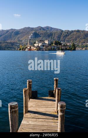 San Giulio Island im Orta-See im Piemont, Italien. Berge, Boot segeln auf blauem Wasser, Kirche, Kloster, andere Gebäude und Pier im Vordergrund Stockfoto