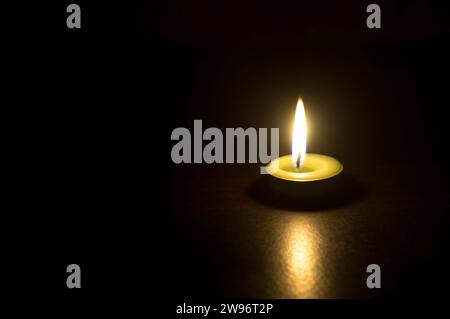 Eine einzelne brennende Kerzenflamme oder Licht leuchtet auf einer kleinen grünen Kerze auf schwarzem oder dunklem Hintergrund auf dem Tisch in der Kirche zu Weihnachten, Beerdigung oder Erinnerung Stockfoto