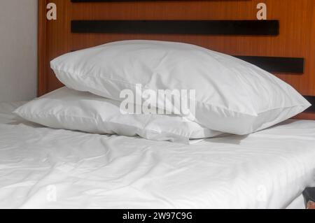 Weiße, unordentliche Bettlaken und zwei Kissen auf dem Bett wurden nach dem Gebrauch der Gäste im Resort oder Hotelzimmer genommen. Stockfoto