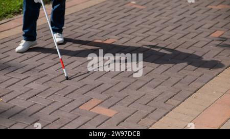 Eine gesichtslose blinde Frau läuft mit einem Stock die Straße entlang. Stockfoto