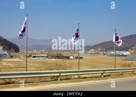 Mungyeong City, Südkorea - 10. Februar 2021: Drei koreanische Flaggen sind stolz auf Fahnenmasten entlang einer Straße im Viertel Jeomchon, mit einem Stockfoto