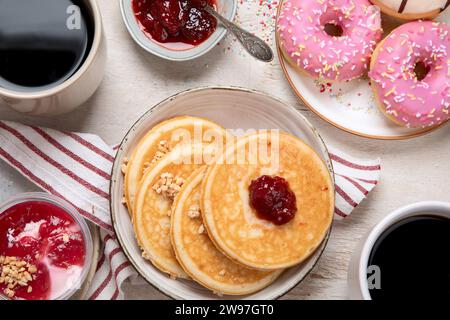 Tisch mit verschiedenen amerikanischen Keksen, Donuts, Pfannkuchen und Kaffeetassen auf weißem Hintergrund. Draufsicht. Stockfoto