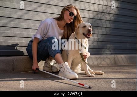 Eine blinde Frau geht mit ihrem Blindenhund auf die Straße. Ein Mädchen, das einen labrador umarmt. Stockfoto