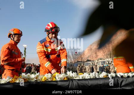 Jishishan, Chinas Provinz Gansu. Dezember 2023. Während einer Gedenkveranstaltung auf einem Platz in der Gemeinde Dahejia im Jishan County, nordwestchinesische Provinz Gansu, legen Menschen Blumen, um die Erdbebenopfer 2023 zu betrauern. Ein Erdbeben der Stärke 6,2 erschütterte das Jishan County in der Provinz Gansu am 18. Dezember. Quelle: Fang Xin/Xinhua/Alamy Live News Stockfoto