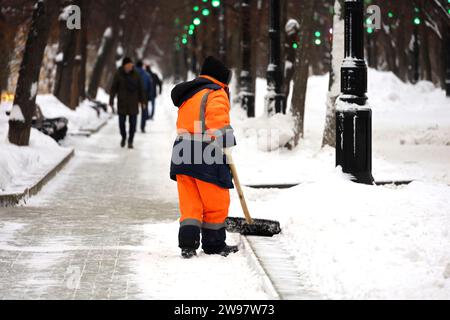 Kommunaler Arbeiter in Uniform mit Schaufel räumt Schnee auf einem Bürgersteig ab. Frau bei Schneeräumung in der Winterstadt, Straßenreinigung Stockfoto