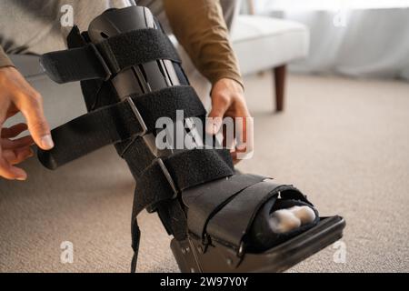 Nahaufnahme eines Verletzungsmannes mit schwarzer Schiene am Bein, der zu Hause auf dem Sofa sitzt und seine Orthese trägt. Sprungfußverletzungen Orthesen Stockfoto