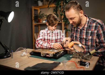 Vater und Sohn verbringen Zeit miteinander, um einen kaputten Laptop mit einem Lötkolben und anderen Reparaturwerkzeugen zu reparieren. Familienurlaub Stockfoto