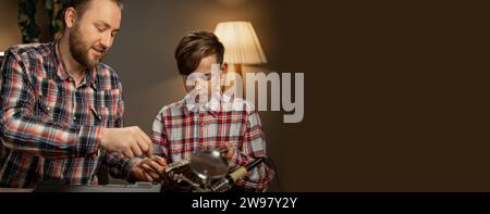 Vater und Sohn zerlegen einen Laptop und reparieren das Mainboard mit einem Schraubendreher. Banner. Stockfoto