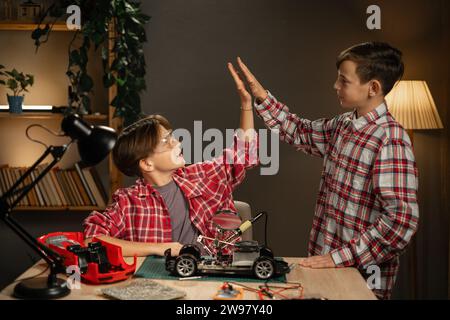 Zwei glückliche Kinder, die zu Hause hohe fünf stehen, feiern Erfolg, gute Zusammenarbeit Ergebnis in ihrem Roboterprojekt Stockfoto