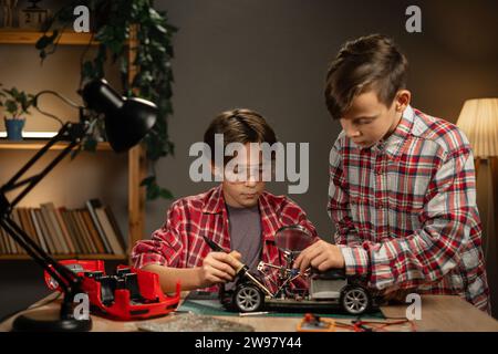 Zwei Teenager-Schüler, die Drähte in Hobbyelektronik-Projekt löten. Jungs, die an einem kaputten Auto in ihrem Zimmer arbeiten. Bildung Stockfoto