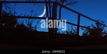 Eine ruhige nächtliche Szene mit einem klaren Himmel, der von einem brillanten Vollmond beleuchtet wird, mit einem Zaun im Vordergrund Stockfoto