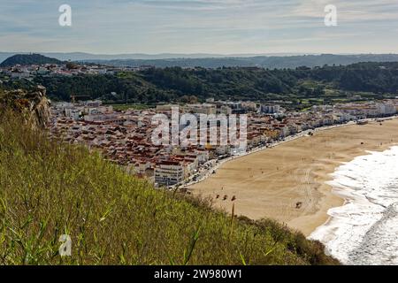 Ein atemberaubender Blick aus der Luft auf einen Sandstrand mit kristallklarem, blauem Wasser des Ozeans, das sich gegen die Küste in der Nähe eines grasbewachsenen Hügels im Hintergrund schlägt Stockfoto