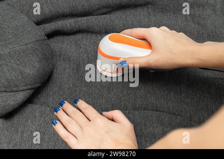 Die Frau entfernt Pillen aus der Kleidung mit einem Pillen-Entferner. Maschine zum Entfernen der Pellets. Die Pillen aus der Kleidung entfernen Stockfoto