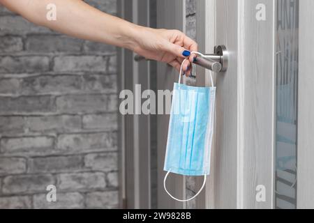 Weibliche Hand hängt eine medizinische Maske am Türgriff Stockfoto