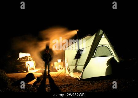 Ein Mann steht in der Silhouette vor Rauch, der aus dem Ofen eines Zeltes kommt. Stockfoto