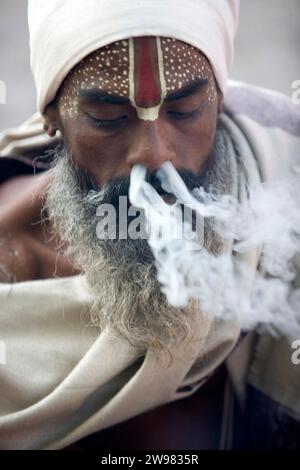 Ein Sadhu, der eine Mischung aus Tabak und Haschisch, oder charas, in einer geraden Tonpfeife raucht, die Chillum genannt wird. Stockfoto