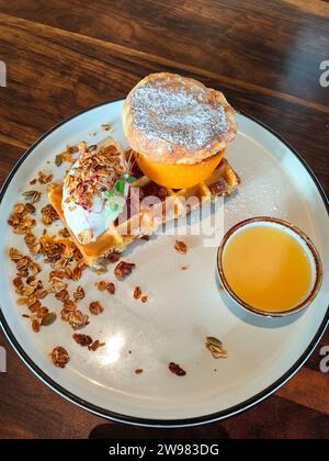 Ein weißer Teller gefüllt mit frisch zubereiteten Waffeln, einem Glas frisch gepressten Orangensaft und einer Handvoll Nüsse Stockfoto