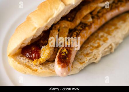 Bosna oder Bosner scharfer Hot Dog nach österreichischer Art mit gegrillter Bratwurst, Zwiebeln, Tomatenketchup und Curry im selektiven Fokus Stockfoto