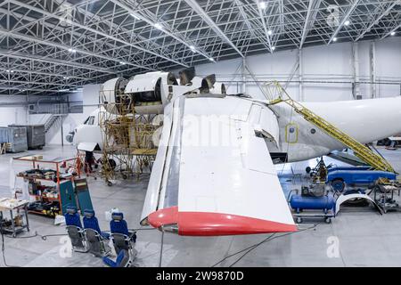 Weißes Transportflugzeug im Flugzeughangar. In Wartung befindliches Luftfahrzeug. Überprüfung mechanischer Systeme für den Flugbetrieb Stockfoto