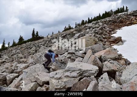 Junger Mann, der einen Nike Rucksack trägt, Felsbrocken klettert und den Berg des Medicine Bow Peak hinaufwandert Stockfoto