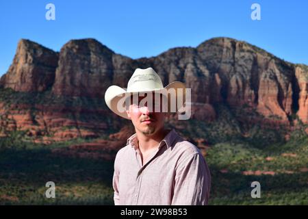 Mann in rosa Hemd und mit einem weißen Cowboyhut mit der Landschaft von Sedona in der Wüste von Arizona als Hintergrund Stockfoto