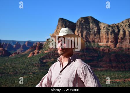 Mann in rosa Hemd und mit einem weißen Cowboyhut mit der Landschaft von Sedona in der Wüste von Arizona als Hintergrund Stockfoto