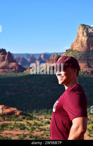 Junger kaukasischer Mann mit rotem T-Shirt und roter Mütze, der auf Bell Rock steht und die Landschaft von Sedona in der Wüste von Arizona überblickt Stockfoto