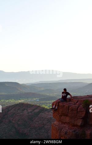 Person, die vom Cathedral Rock in Sedona aus auf einem Steinvorsprung sitzt und die Wüstenlandschaft von Arizona überblickt Stockfoto