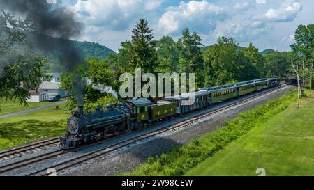 Ein Blick aus der Vogelperspektive auf einen Schmalspurzug, der sich nähert, Rauch bläst, an einem sonnigen Sommertag vorbei an Kohlenbehältern Stockfoto